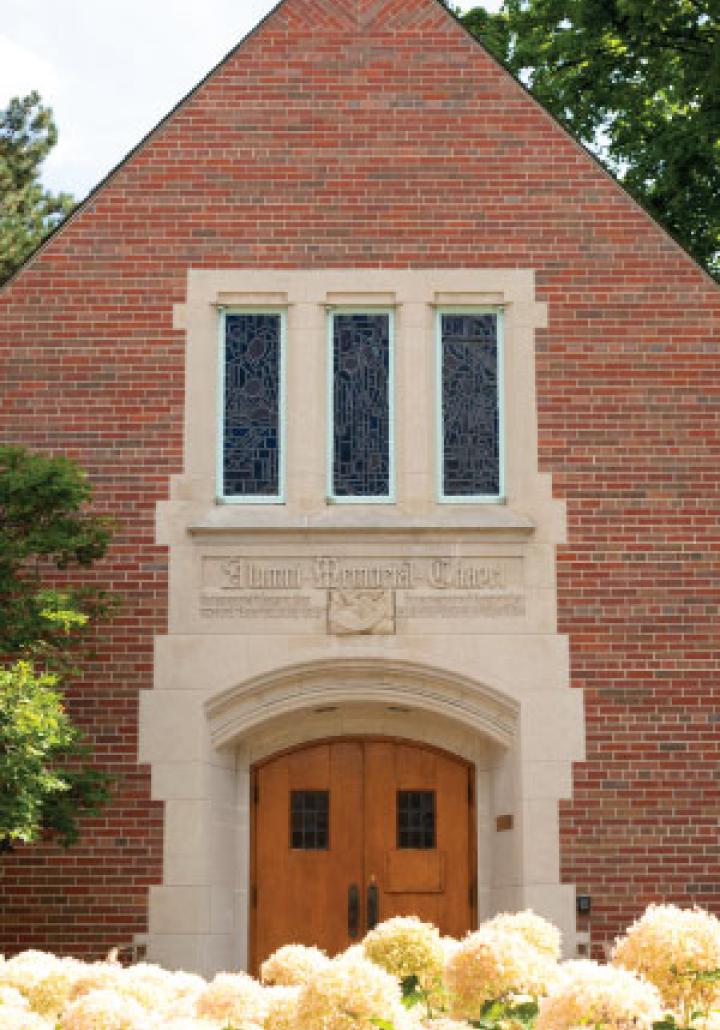 Front view of the MSU Chapel with stained glass windows and a wooden double door entrance, framed by blooming hydrangeas.